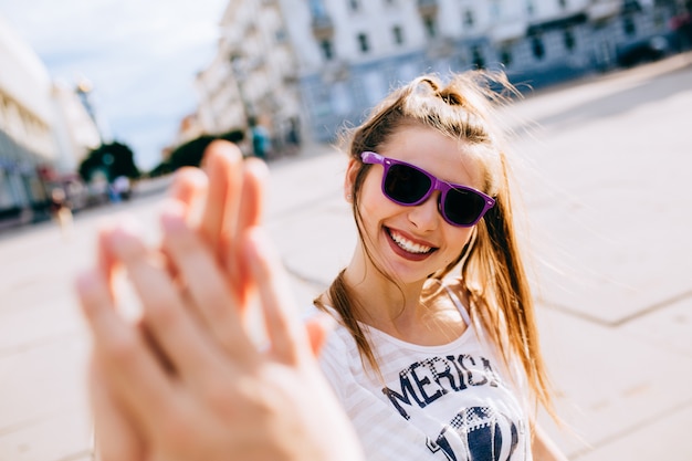 Lächelnde Schönheit in der Sonnenbrille, die dem Freund beim Gehen auf der Stadt Hoch fünf gibt