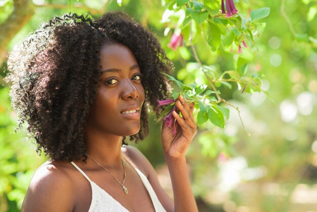 Lächelnde schwarze Frau, die Blumen im Park riecht