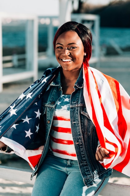 Lächelnde schwarze Frau eingewickelt in der amerikanischen Flagge