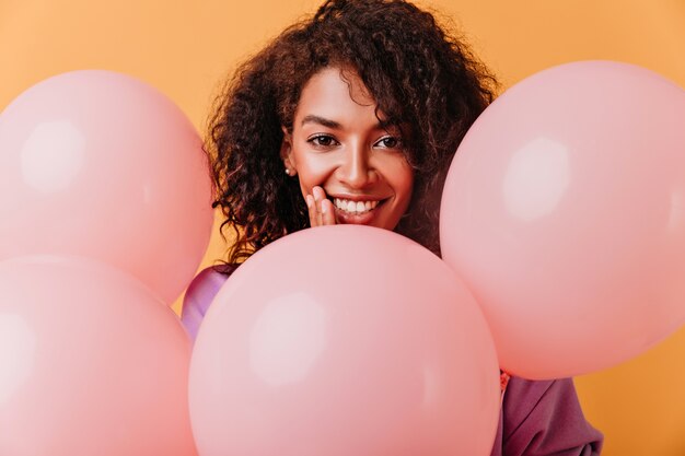 lächelnde schwarze schöne Frau mit Luftballons. Geburtstagskind isoliert auf Orange.