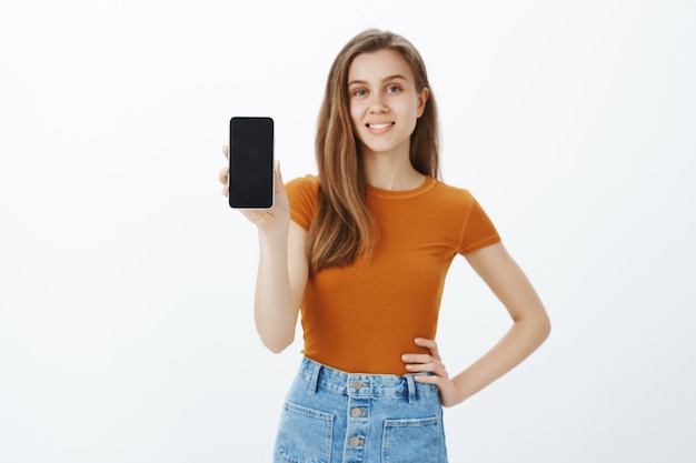Lächelnde selbstbewusste junge Frau geben Ratschläge, zeigen Smartphone-Bildschirm, demonstrieren Anwendung oder kaufen