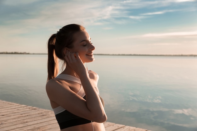 Lächelnde Sportdame am Strand, die Musik hört