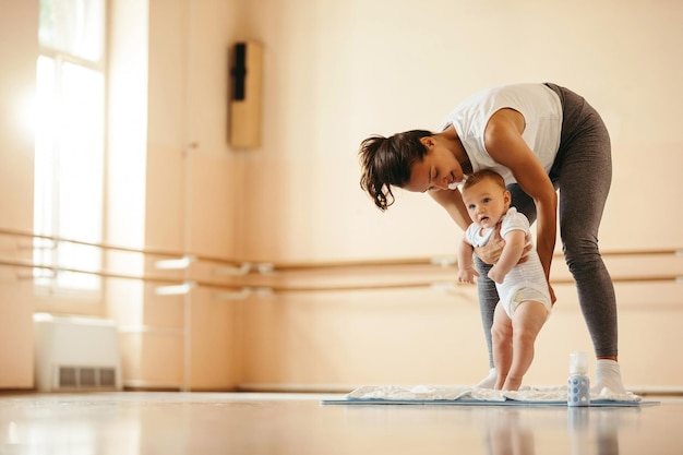 Kostenloses Foto lächelnde sportliche mutter, die sich mit ihrem kleinen jungen amüsiert, während sie ihm beibringt, in einem fitnessstudio zu stehen. kopierraum