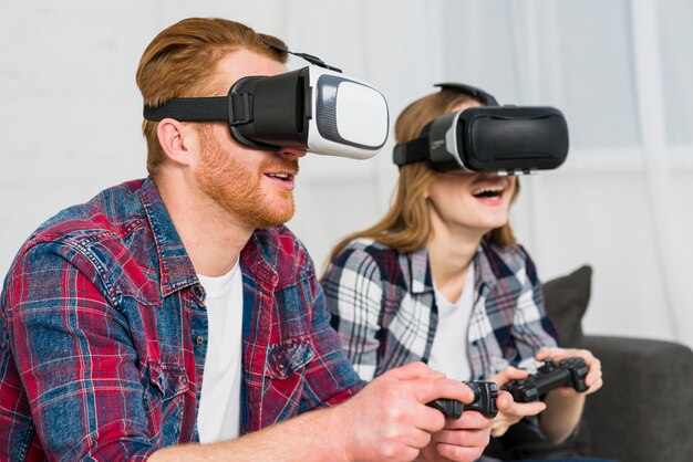 Lächelnde tragende Wirklichkeitsbrillen der jungen Paare, die das Videospiel spielend genießen