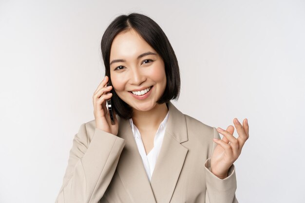 Lächelnde Unternehmensfrau im Anzug, die am Handy spricht und einen Geschäftsanruf auf dem Smartphone hat, das über weißem Hintergrund steht