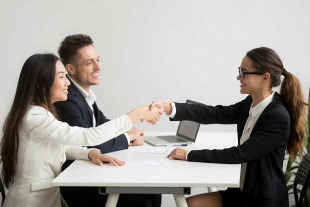 Lächelnde verschiedene Geschäftsfrauen rütteln Hände bei der Gruppensitzung, Abkommenkonzept