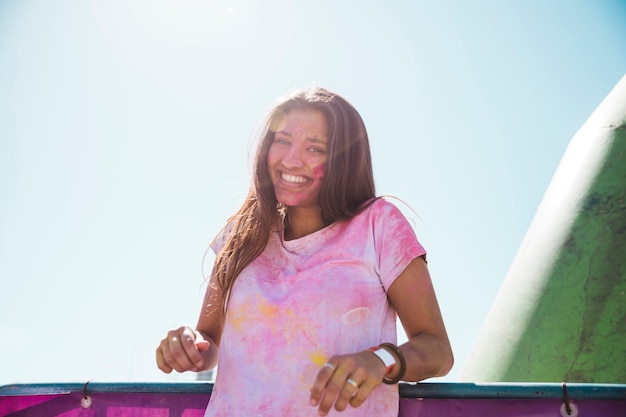 Kostenloses Foto lächelnde verwirrung der jungen frau in holi farbe, die gegen blauen himmel steht