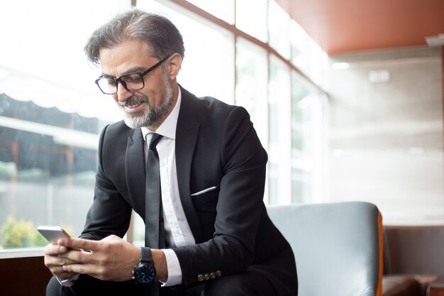 Lächelnder älterer Mann, der Nachricht auf Telefon überprüft