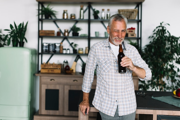 Lächelnder älterer Mann, der sein Auge blinzelt, Bierflasche in der Hand halten