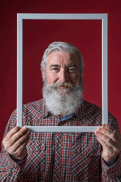 Lächelnder älterer Mann, der weißen Grenzrahmen gegen farbigen Hintergrund hält
