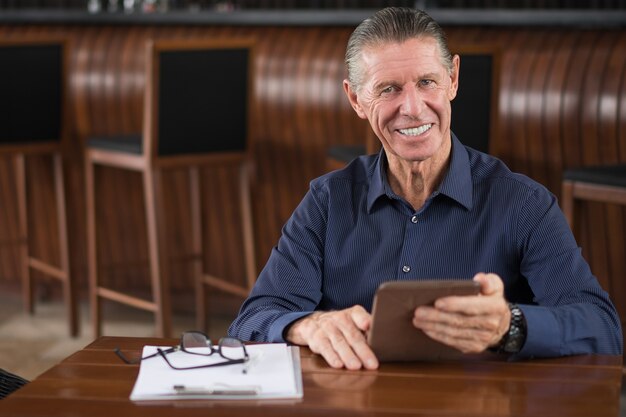 Lächelnder älterer Mann mit Digital-Tablette in Cafe