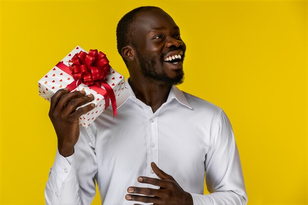 Lächelnder afrikanischer Mann, der weg schaut und eine Geschenkbox hält