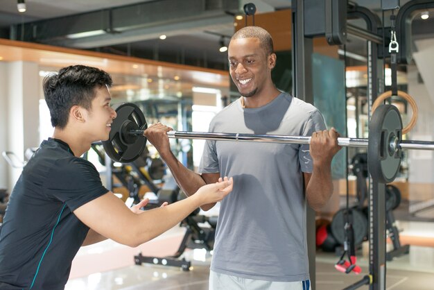 Lächelnder anhebender Barbell des schwarzen Mannes mit persönlichem Trainer