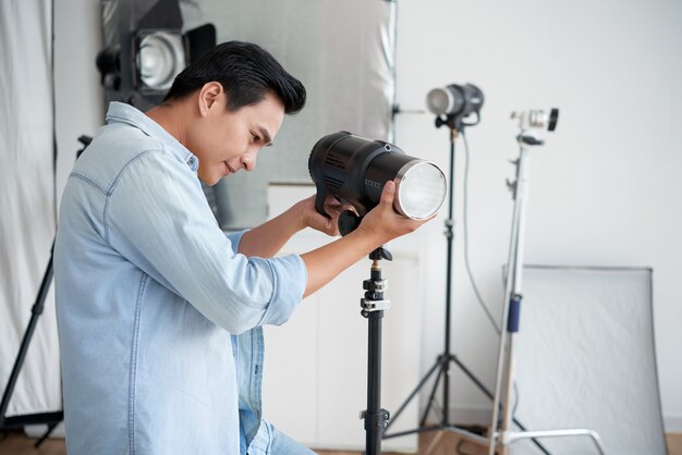 Lächelnder asiatischer Fotograf, der Beleuchtungslampe im Berufsstudio justiert