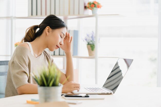 Lächelnder asiatischer Frauenarbeitslaptop der schönen Junge auf Schreibtisch im Wohnzimmer zu Hause