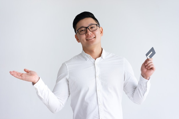 Lächelnder asiatischer Mann, der Kreditkarte hält und oben Hand wirft
