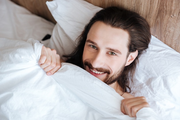 Lächelnder bärtiger junger Mann, der im Bett liegt