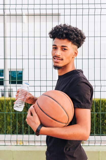 Lächelnder Basketball-Spieler mit der Flasche Wasser Kamera betrachtend