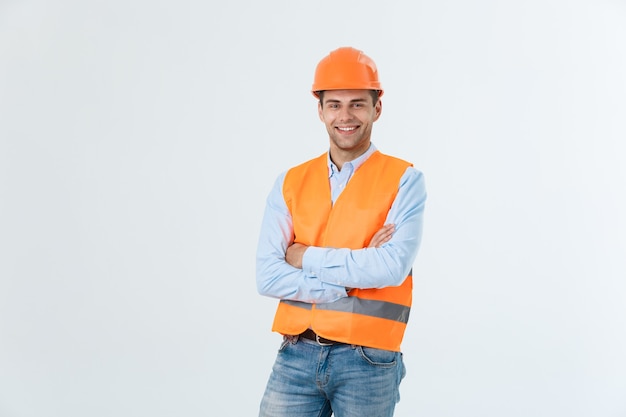 Lächelnder Bauingenieur, der mit verschränkten Armen posiert. Auf grauem Hintergrund isoliert.