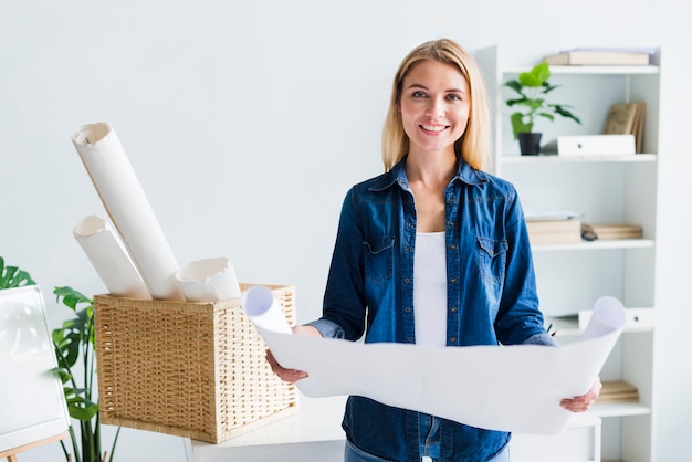 Kostenloses Foto lächelnder blonder frauendesigner mit großem ausgerolltem papierblatt