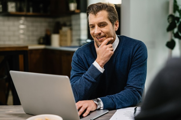 Lächelnder erwachsener Geschäftsmann der Mitte, der eine E-Mail liest, während er am Computer arbeitet