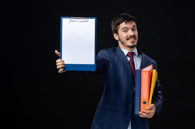 Lächelnder Erwachsener im Anzug, der mehrere Dokumente hält und eines von ihnen an einer isolierten dunklen Wand zeigt