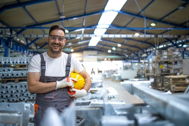 Lächelnder Fabrikarbeiter mit Schutzhelm, der in der Fabrikproduktionslinie steht