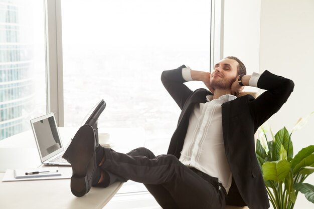 Lächelnder Geschäftsmann, der am Arbeitsplatz im modernen Büro sich entspannt.