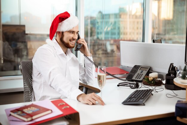 Lächelnder Geschäftsmann, der am Telefon am Worplace-Weihnachtstag spricht.