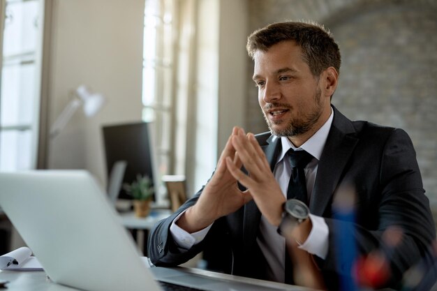 Lächelnder Geschäftsmann, der eine E-Mail auf dem Laptop liest, während er im Büro arbeitet