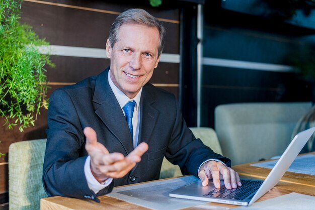 Lächelnder Geschäftsmann, der Handgeste mit Laptop über Schreibtisch im Restaurant macht