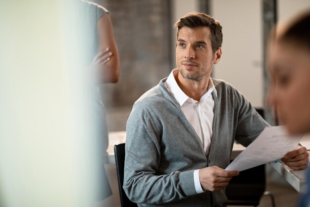 Lächelnder Geschäftsmann, der Papierkram hält, während er einer Präsentation im Büro zuhört