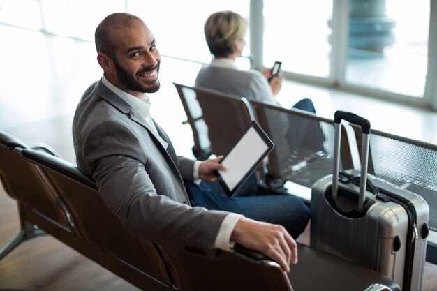Lächelnder Geschäftsmann mit der digitalen Tablette, die im Wartebereich sitzt