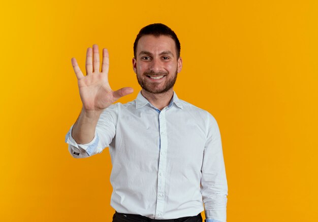 Lächelnder gutaussehender Mann gestikuliert fünf mit der Hand, die auf orange Wand lokalisiert wird