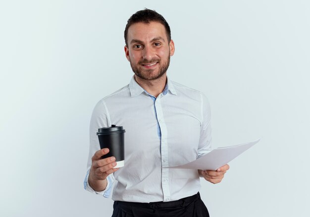 Lächelnder gutaussehender Mann hält Kaffeetasse und Papierblätter lokalisiert auf weißer Wand