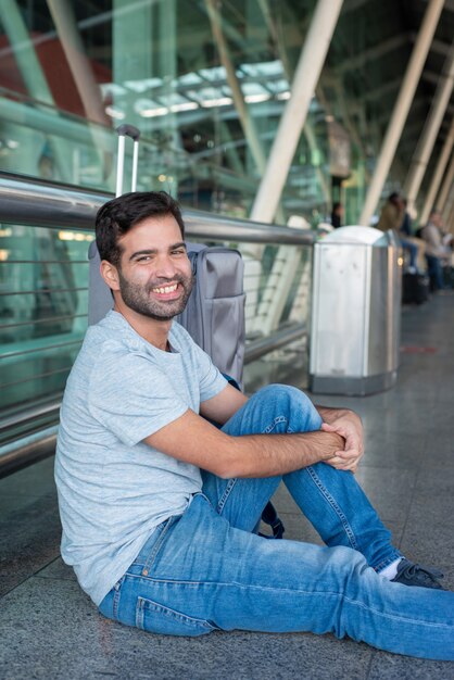 Lächelnder hispanischer Mann, der auf Boden am Flughafen sitzt