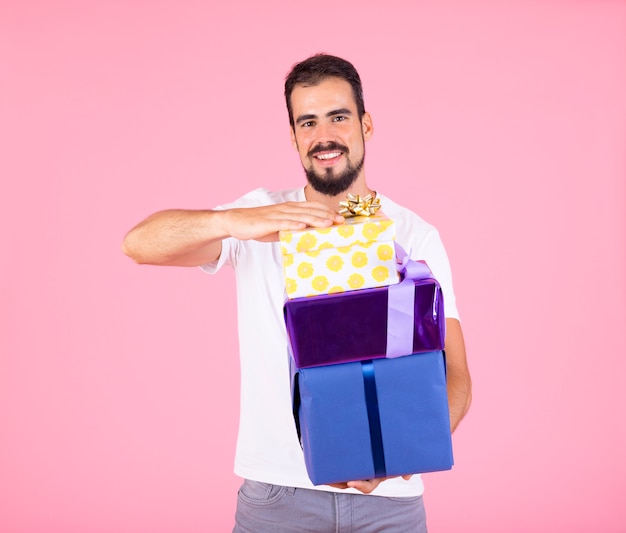 Lächelnder Holdingstapeln des jungen Mannes Geschenkboxen gegen rosa Hintergrund