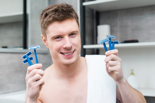 Kostenloses Foto lächelnder hübscher hemdloser junger mann, der in der hand viel blaues rasiermesser hält