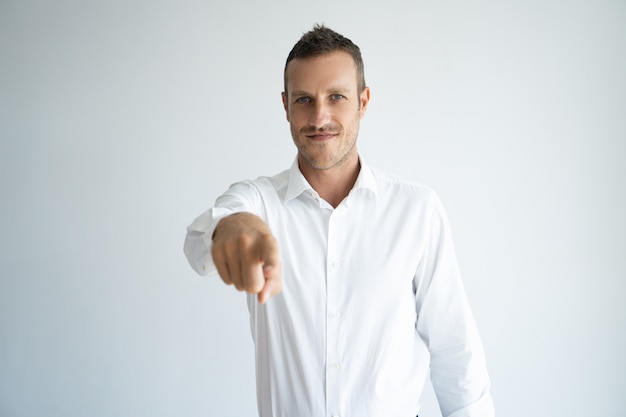 Lächelnder hübscher junger Arbeitgeber, der mit dem Finger auf Kamera beim Wählen Sie zeigt.