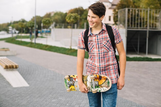 Lächelnder Jugendlicher, der mit Skateboard geht