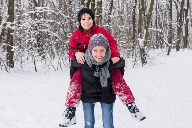 Lächelnder Junge, der Doppelpol mit seiner Mutter im Winter am Wald genießt