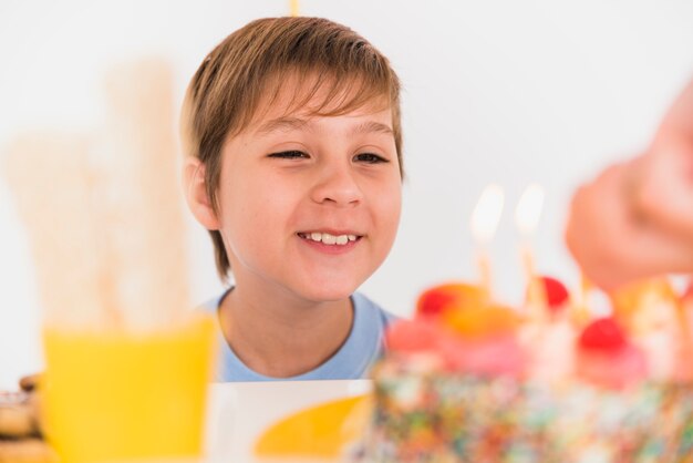 Lächelnder Junge, der geschmackvollen Geburtstagskuchen mit brennenden Kerzen betrachtet