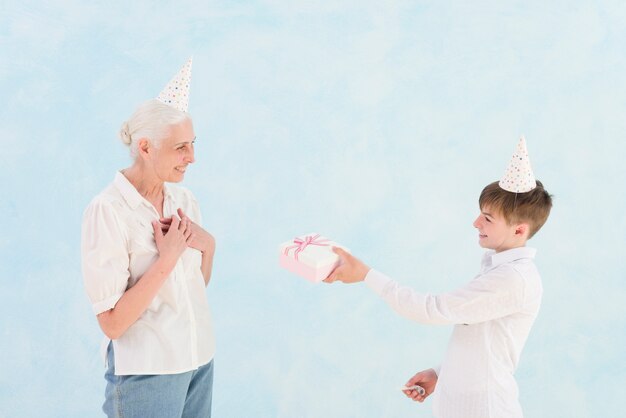 Lächelnder Junge, der seiner Großmutter vor blauem Hintergrund Geburtstagsgeschenk gibt