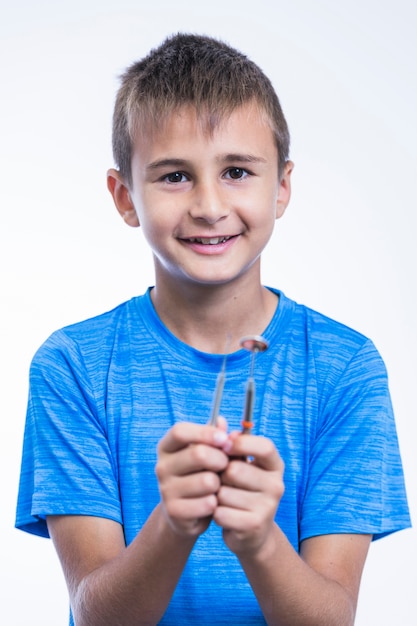 Lächelnder Junge, der Skalator und zahnmedizinischen Spiegel auf weißem Hintergrund hält