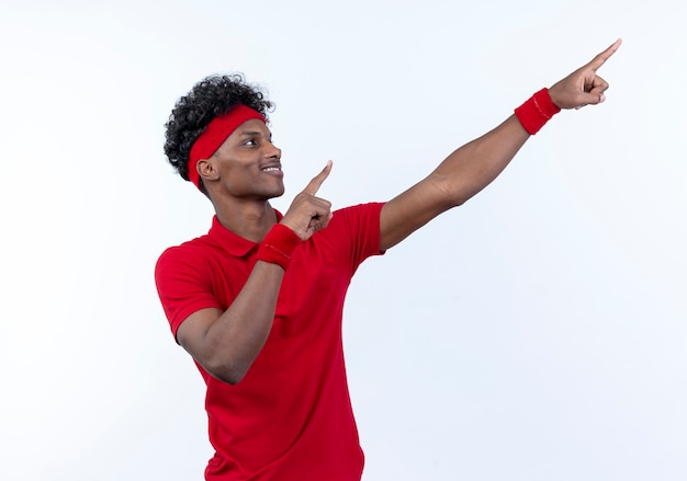 Lächelnder junger afroamerikanischer sportlicher Mann, der Stirnband und Armbandpunkte an der Seite trägt, lokalisiert auf Weiß