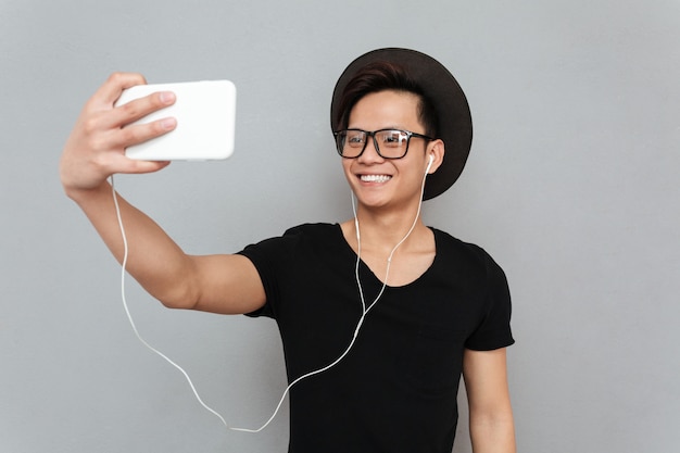 Lächelnder junger asiatischer Mann, der Musik hört und Selfie macht