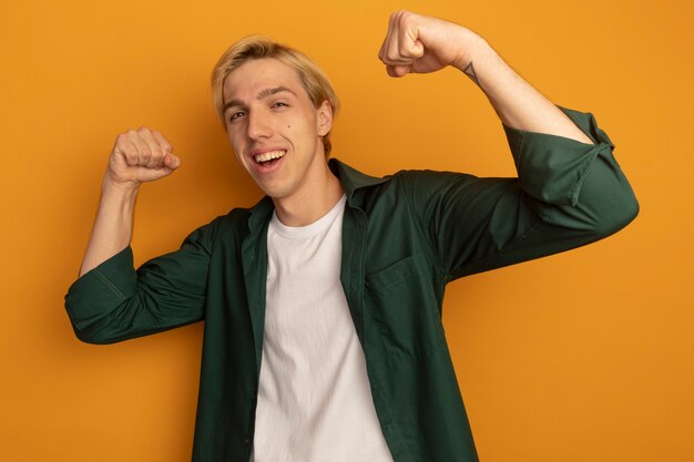 Lächelnder junger blonder Kerl, der grünes T-Shirt trägt, das starke Geste zeigt