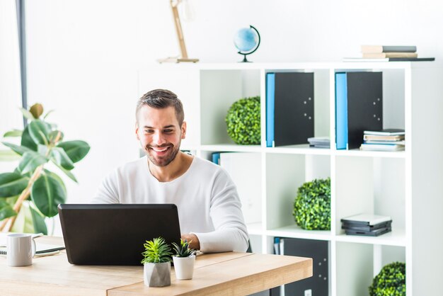 Lächelnder junger Geschäftsmann, der Laptop im Büro verwendet