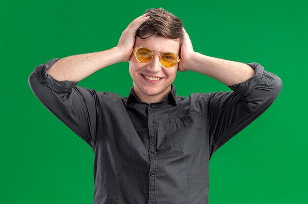 Lächelnder junger kaukasischer Junge in Sonnenbrille, der sich die Hände auf den Kopf legt und in die Kamera schaut