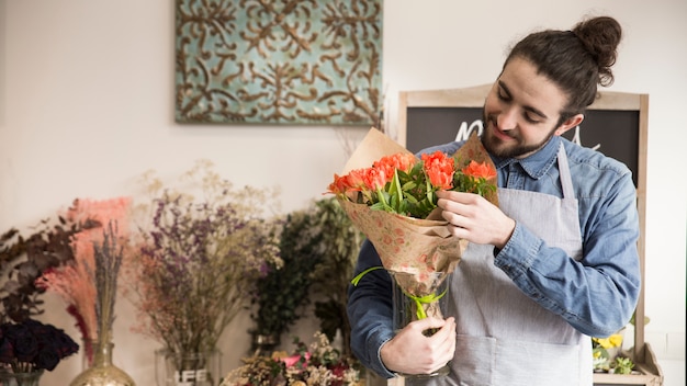 Lächelnder junger männlicher Florist, der Blumen im Blumenstrauß betrachtet